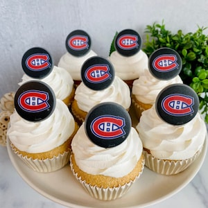 Op de afbeelding: Een bord met cupcakes versierd met witte frosting en ronde zwarte en rode hockeyteamlogo's.
