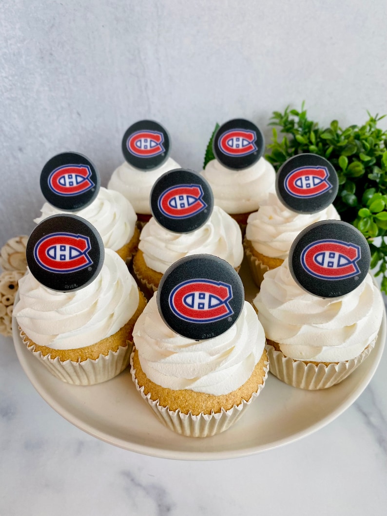 Op de afbeelding: Een bord met cupcakes versierd met witte frosting en ronde zwarte en rode hockeyteamlogo's.