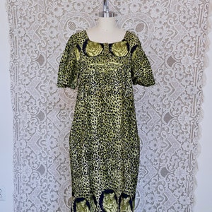 Puede incluir: Un vestido maxi verde y negro con estampado de leopardo y caras de tigre en el dobladillo. El vestido tiene un escote cuadrado y mangas cortas.