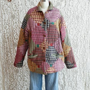 May include: A patchwork quilted jacket in a variety of colors, including pink, red, yellow, and blue. The jacket has a button-up front, two pockets, and a collar. The jacket is displayed on a mannequin with blue jeans.