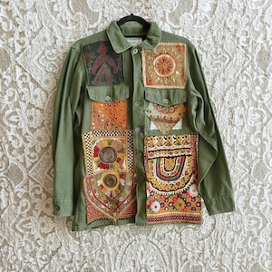 May include: An olive green button-down jacket featuring a variety of colorful, embroidered fabric patches sewn onto the front. The patches include intricate floral and geometric patterns, metallic thread accents, and small circular mirrors.