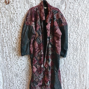 May include: A long-sleeved coat featuring a patchwork design in shades of deep red, burgundy, and black. The garment has a collared neckline, a button-front closure, and solid black panels along the sides and sleeves with a textured finish.