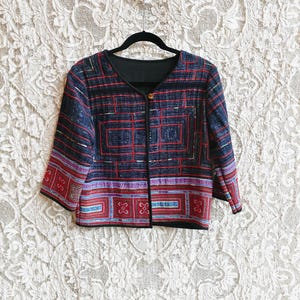 May include: A colorful, patterned jacket with a black collar and sleeves. The jacket features a geometric design in red, blue, and purple. The jacket is hanging on a black hanger.