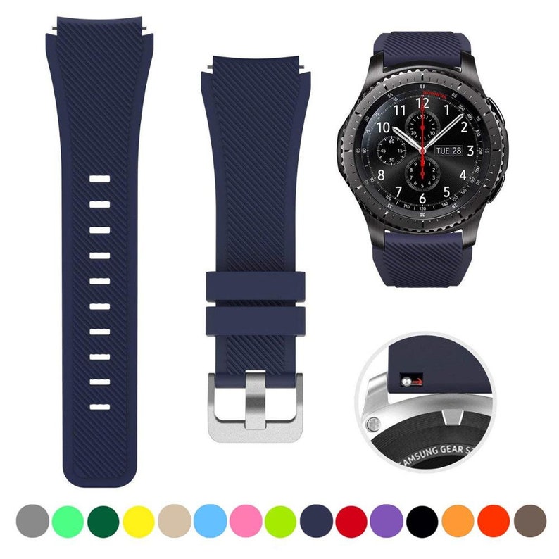 May include: A dark blue silicone watch band with a diagonal ribbed texture, featuring a silver-toned metal buckle and a quick-release pin mechanism. The band is shown attached to a black smartwatch with a round analog-style digital face.