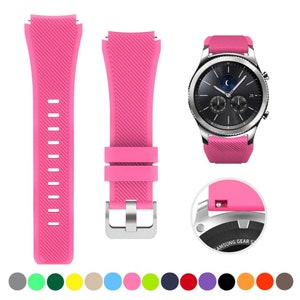 May include: A bright pink silicone watch band with a diagonal ribbed texture, featuring a silver-toned metal buckle and a quick-release pin mechanism. The band is shown attached to a silver-cased smartwatch with a black circular analog display.
