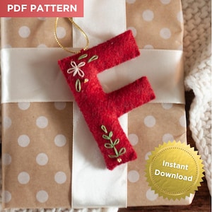 May include: A red felt Christmas ornament in the shape of the letter "F", adorned with embroidered floral details. The ornament hangs from a gold string and is presented on a wrapped gift with a white ribbon. The words "PDF PATTERN" and "Instant Download" are visible.