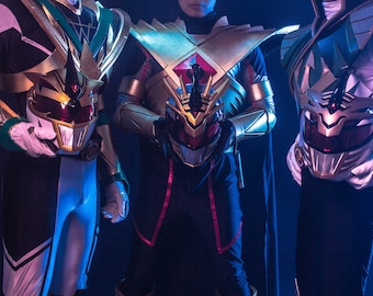 May include: Three figures in gold, white, and black superhero costumes. Each costume features a helmet with a distinctive animal-like design. The costumes have gold accents and armor-like shoulder pieces. The figures are standing in a dimly lit setting.