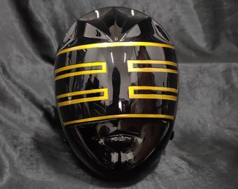 May include: Black plastic helmet with gold accents. The helmet has a visor and a design of horizontal lines on the front.