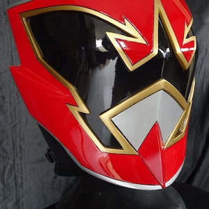 Op de afbeelding: Rode, zwarte en gouden plastic helm met een gestileerd ontwerp. De helm heeft een zwart vizier en een gouden rand.