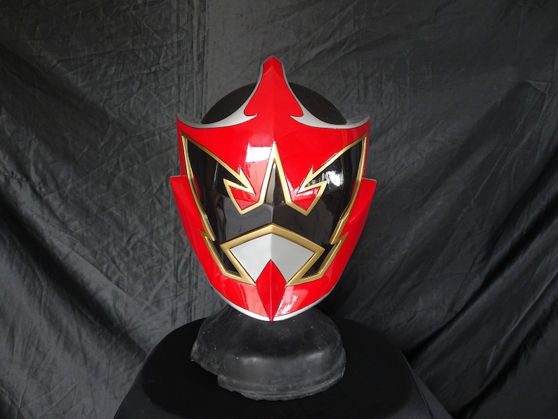 Op de afbeelding: Rode, zwarte en gouden Power Rangers helm met een stervormig ontwerp. De helm is gemaakt van plastic en heeft een glanzende afwerking.