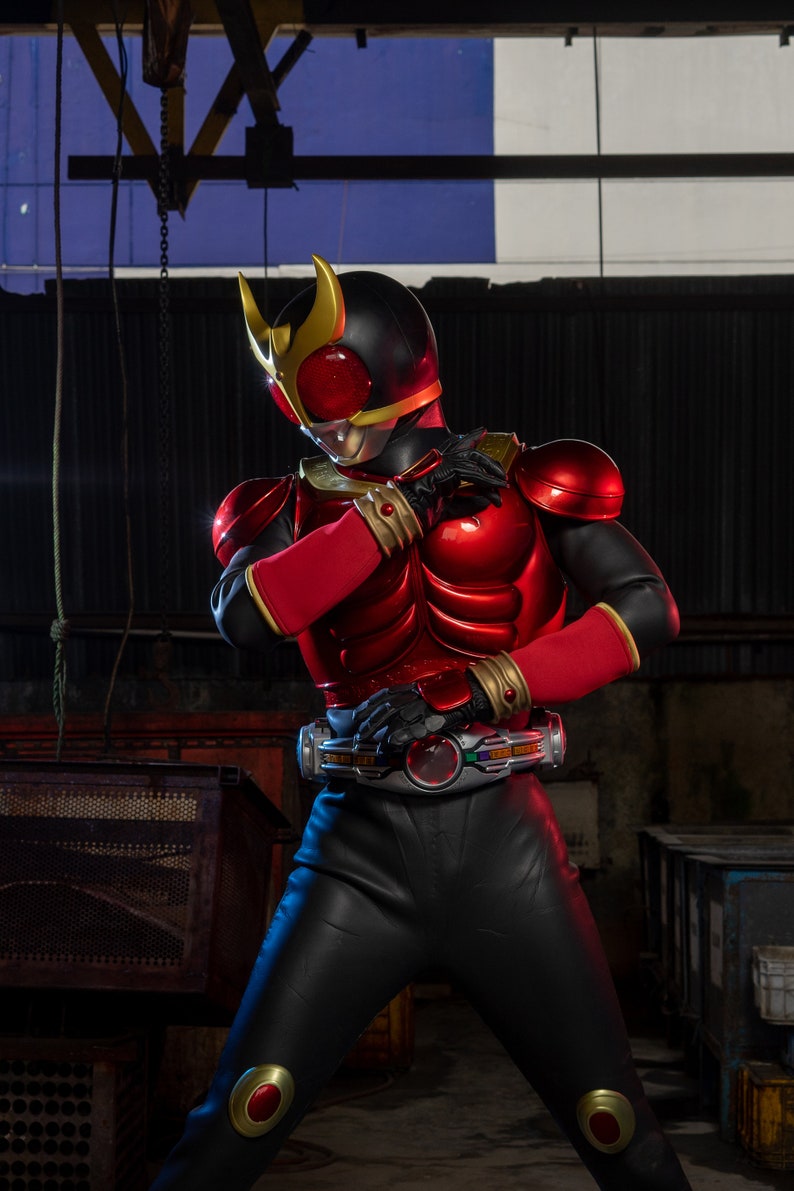 May include: A red and black superhero costume with gold accents. The costume features a helmet with gold horns, a red chest plate, and black gloves. The belt has a circular buckle with a colorful design. The suit is made of a shiny material.