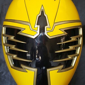 Op de afbeelding: Gele Power Ranger helm met een zwart vizier en gouden accenten. De helm heeft een bliksemontwerp op de bovenkant en zijkanten.