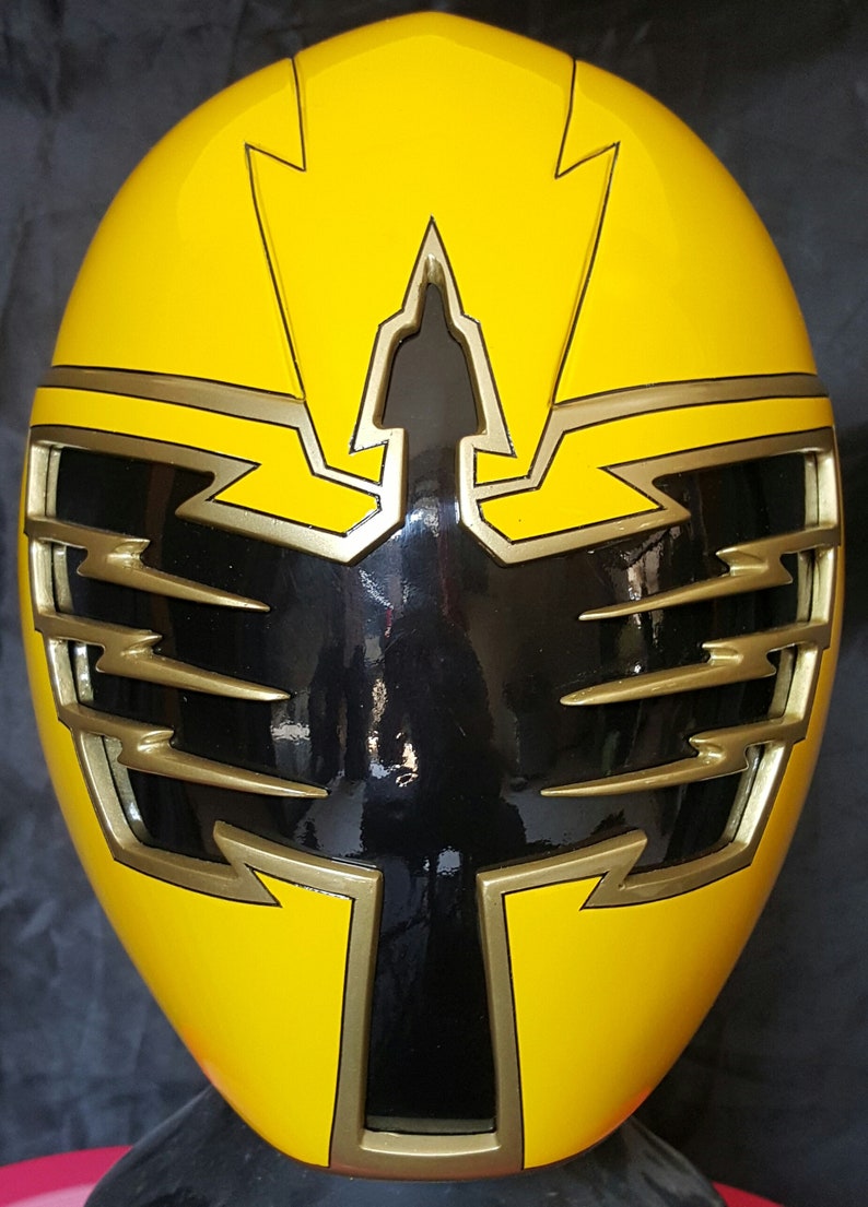 Op de afbeelding: Gele Power Ranger helm met een zwart vizier en gouden accenten. De helm heeft een bliksemontwerp op de bovenkant en zijkanten.