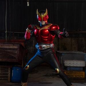 May include: A red and black superhero costume with gold accents. The costume features a helmet, chest armor, and black pants. The superhero is in a fighting stance, with one hand raised in a fist and the other in a thumbs-up gesture.