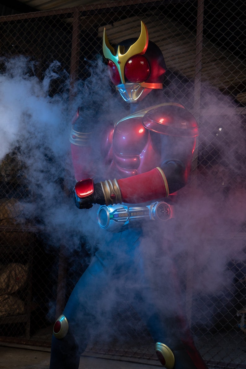 May include: A red and gold superhero costume with a helmet, chest armor, and arm gauntlets. The costume features a red visor and gold accents. The figure is surrounded by blue and white smoke.