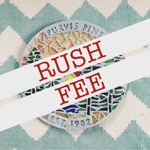 May include: A round, mosaic-style tile with the text "Purvis Pine" and "Est. 1932" in a white font. The tile has a colorful mosaic design with a red, white, and blue color scheme. The text "Rush Fee" is written in red across the tile.