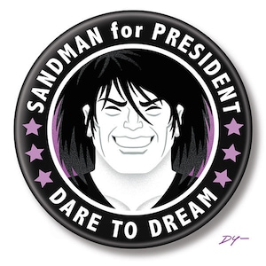 May include: A black and white button with a purple border. The button features a cartoon image of a man with black hair and a white face. The text on the button reads "SANDMAN for PRESIDENT DARE TO DREAM".