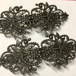 May include: Two ornate metal hair clips with a filigree design. The clips are a dark bronze colour and have a floral pattern.