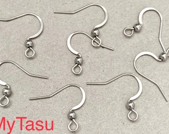 May include: Close-up of several silver-colored earring hooks. Each hook has a curved design with a small ball and a loop at the bottom. The hooks are arranged on a light gray surface. The text "My Tasu" is in red in the bottom left corner.