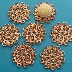 May include: Six rose gold metal filigree embellishments with a circular design. The embellishments have a delicate, intricate pattern and a hole in the center.