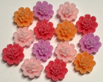 Könnte beinhalten: Sortiment von 14 Kunststoff-Blumenverzierungen in verschiedenen Rosatönen, Orange- und Lilatönen. Jede Blume hat ein mehrschichtiges Design mit mehreren Blütenblättern.