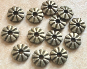 May include: A group of 14 silver metal beads with a decorative flower design. The beads have a hole in the center for stringing.