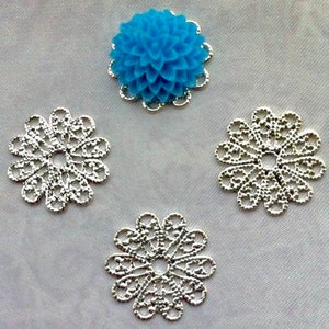 May include: Four silver filigree embellishments with a blue flower embellishment in the center.