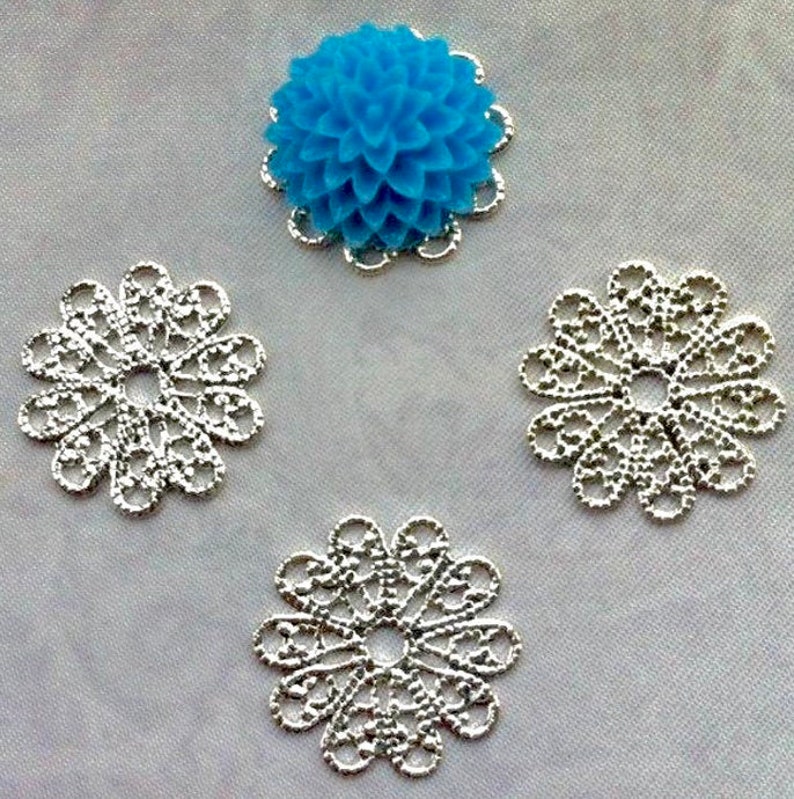 May include: Four silver filigree embellishments with a blue flower embellishment in the center.