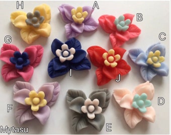 Könnte beinhalten: Zehn verschiedene farbige Polymer Clay Blumen Charms mit einer Vielzahl von Blumendesigns. Die Blumen sind alle etwa 2,5 cm im Durchmesser. Die Farben umfassen Gelb, Lila, Rosa, Rot, Blau und Weiß.