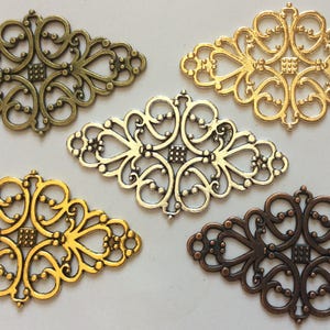 Puede incluir: Cuatro adornos de filigrana metálica adornados con diferentes acabados: oro, plata y bronce. Cada pieza tiene forma de diamante con intrincados diseños florales.