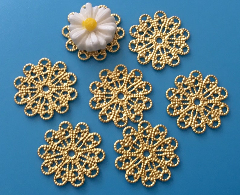 May include: Six gold metal filigree embellishments with a daisy-shaped design. The embellishments are approximately 1 inch in diameter.