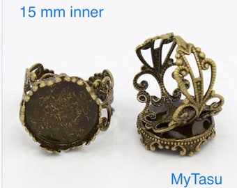 Op de afbeelding: Twee antieke, goudkleurige metalen ringblanken met een binnendiameter van 15 mm. Elke ringblank heeft een decoratief filigraanontwerp en een ronde bezel voor het instellen van een cabochon.