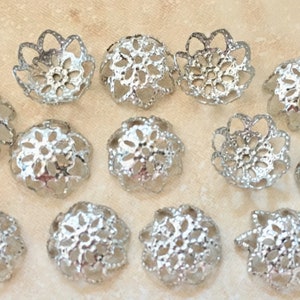 May include: A collection of 14 silver filigree bead caps. The caps are round and feature a delicate, intricate design. They are ideal for adding a touch of elegance to jewellery projects.
