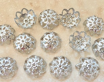 May include: A collection of 14 silver filigree bead caps. The caps are round and have a delicate, intricate design. They are perfect for adding a touch of elegance to jewelry projects.