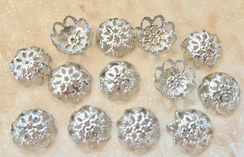 May include: A collection of 14 silver filigree bead caps. The caps are round and feature a delicate, intricate design. They are ideal for adding a touch of elegance to jewellery projects.