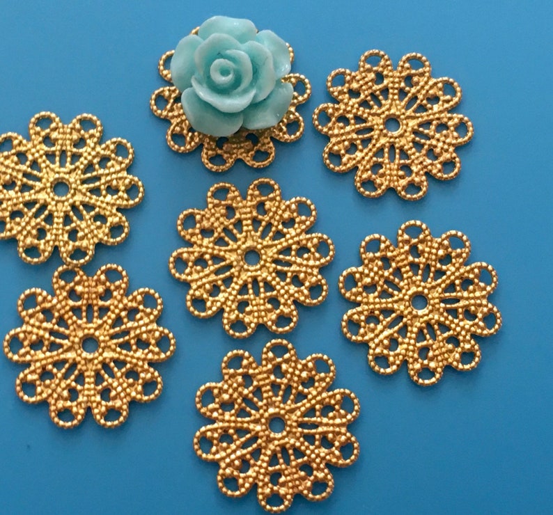 May include: Six gold metal filigree embellishments with a light blue flower embellishment in the center.