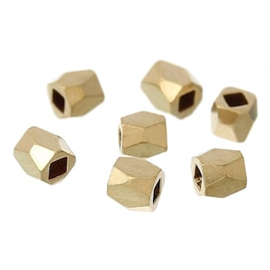 May include: A group of seven gold-colored faceted beads with square holes. The beads are scattered on a white background.