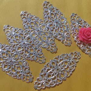 May include: Five silver filigree metal embellishments in the shape of leaves with a pink flower in the center of one of the leaves.