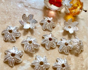 May include: Silver tone metal flower-shaped bead caps with a starburst design. The caps are approximately 1 inch in diameter and have a hole in the center for stringing.