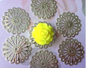 May include: Six silver metal decorative embellishments with a circular, lacy design. The embellishments have a raised center with a small circle in the middle. The embellishments are arranged in a circle around a yellow flower.
