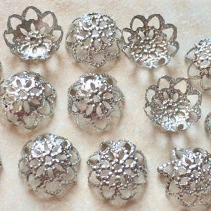 May include: A collection of 12 silver filigree bead caps featuring a delicate floral design. The caps are ideal for adding a touch of elegance to jewellery projects.