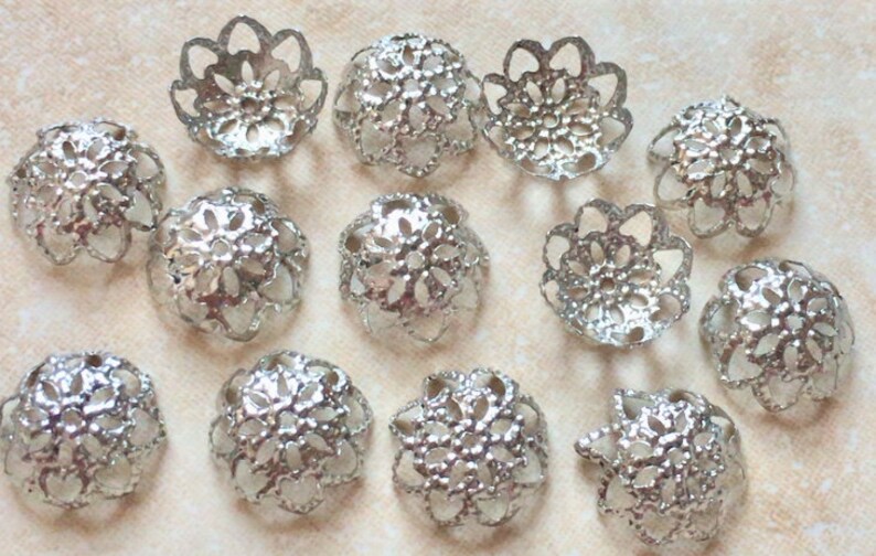 May include: A collection of 12 silver filigree bead caps featuring a delicate floral design. The caps are ideal for adding a touch of elegance to jewellery projects.