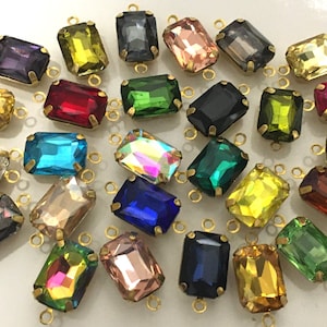 May include: Assortment of colorful glass rectangular beads with gold metal loops. The beads are in various colors, including red, blue, green, yellow, and clear.