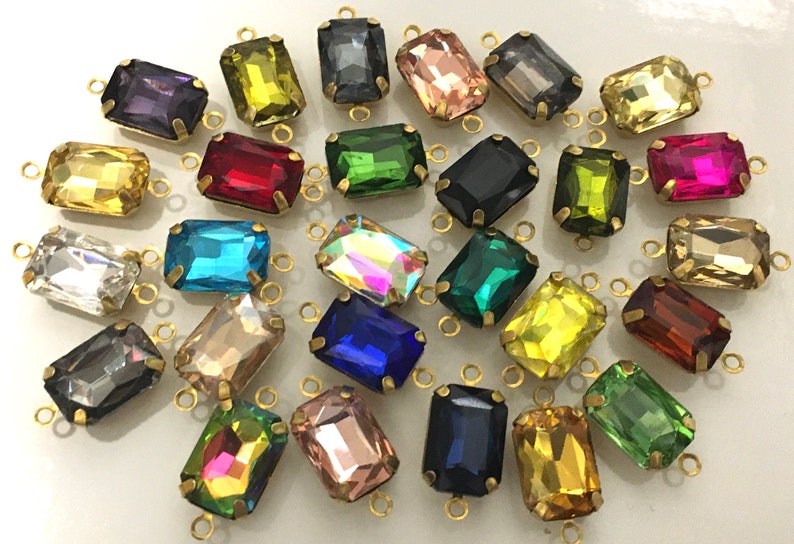 May include: Assortment of colorful glass rectangular beads with gold metal loops. The beads are in various colors, including red, blue, green, yellow, and clear.