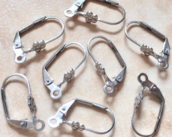 Könnte beinhalten: Acht silberfarbene Ohrring-Clip-Verschlüsse mit Blumenmuster. Die Verschlüsse sind aus Metall und haben eine glatte Oberfläche.