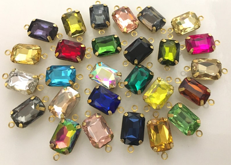 May include: Assortment of colorful glass rectangular beads with gold metal loops. The beads are in various colors, including red, blue, green, yellow, and pink.
