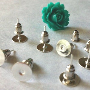 May include: Silver earring backs with a round, flat back and a post with a small, round head. There are eight earring backs in the image.
