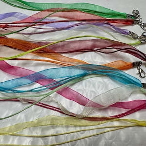May include: A collection of multi-colored organza ribbon necklaces, each featuring a silver-tone lobster claw clasp. The ribbons come in various hues including green, red, purple, white, orange, blue, pink, and yellow, with thin cords.