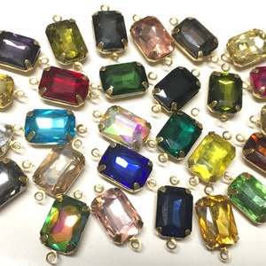 May include: Assortment of colorful glass rectangular beads with gold metal loops on each end. The beads are in various colors, including red, blue, green, yellow, and clear.