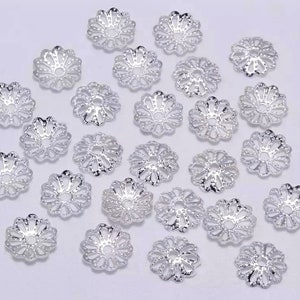 Op de afbeelding: Een verzameling zilverkleurige metalen kralencaps met een decoratief bloemmotief. De caps zijn gerangschikt op een wit oppervlak.